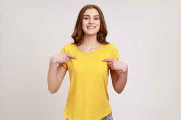 Portrait of charming happy teenager girl in yellow T-shirt smiling and pointing at herself, being...