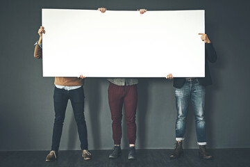 Group of businesspeople holding up a copyspace sign voicing their opinion at work with a grey...