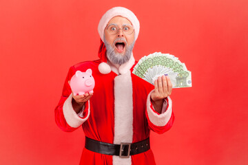Excited shocked elderly man with gray beard wearing santa claus costume standing with euro...
