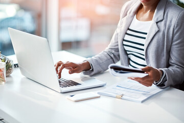 Business woman typing on laptop, reading from notebook and planning a strategy in an office at...