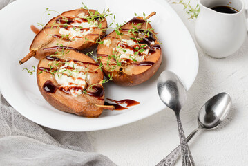 A dish of baked pears with cottage cheese filling and topping in a white plate whith gravy boat and two spoons. Serving fruit sweet dessert close up