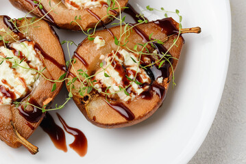 Halves of baked pears filled with cottage cheese and chocolate topping in a white plate.  Macro...