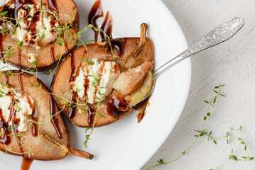 A dish of baked pears stuffed  with cottage cheese and chocolate topping and thyme whith spoon. Eating fruit sweet dessert top view
