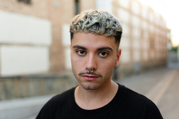 Close up portrait of good-looking serious bearded Caucasian man wearing black casual t-shirt posing isolated on outdoor wall with copy space for your promotional content. 