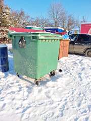 a green plastic container on wheels for garbage stands on the snow