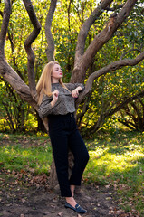 beautiful blonde young smiling girl in tiger blouse staying near great tree in autumn park 