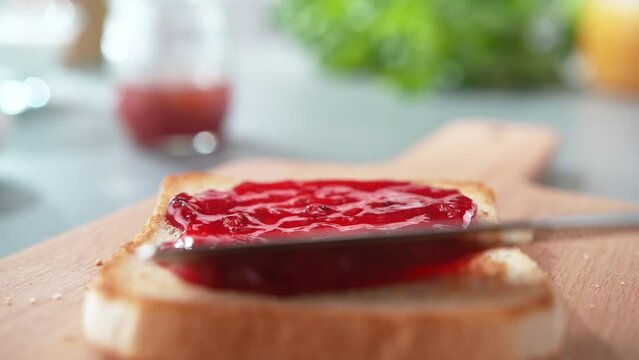 Spreading Red Jam on a Slightly Browned Toast with Table Knife on Cutting Board in Slow Motion