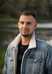 portrait of a man in jeans coat near lake in autumn park