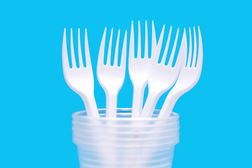Disposable plastic forks and glasses on a black background. Disposable utensils for eating and drinking at a picnic or outdoors. Convenient disposable food and drink accessory