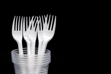 Disposable plastic forks and glasses on a black background. Free space for text. Disposable utensils for eating and drinking at a picnic or outdoors. Taking care of the environment with organic dishes
