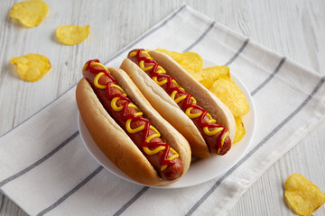 Homemade Hot Dog with Ketchup and Yellow Mustard with Chips on a Plate, low angle view.