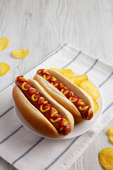 Homemade Hot Dog with Ketchup and Yellow Mustard with Chips on a Plate, side view.