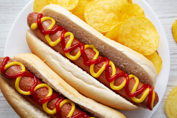 Homemade Hot Dog with Ketchup and Yellow Mustard with Chips on a Plate, top view. Flat lay, overhead, from above. Close-up.
