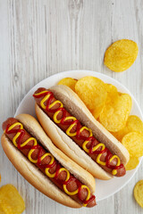 Homemade Hot Dog with Ketchup and Yellow Mustard with Chips on a Plate, top view. Flat lay, overhead, from above. Copy space.