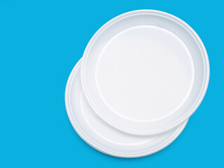 Disposable plastic plates in white on a blue background. Free space for text. Disposable plastic tableware for a picnic or outdoor party. Pollution of nature with plastic and environmental problems