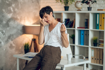 Obraz premium Dark-haired woman in a white shirt sitting in the office and looking tired