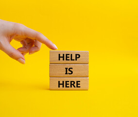 Help is here symbol. Wooden blocks with words Help is here. Beautiful yellow background. Businessman hand. Business and Help is here concept. Copy space.