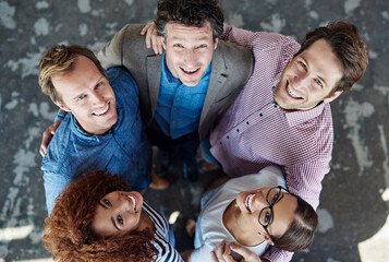 Cheerful, united and diverse group of young business colleagues in collaboration for corporate trust building. Top view of coworkers looking up, smiling and standing close together.