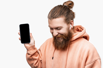 Scandinavian handsome happy man holding phone with a black screen mockup with wireless headphones...