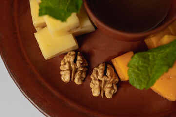 a clay plate with sliced different types of cheese, on a white background, an appetizer 