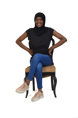 front view of a woman with casual clothing and burka sitting on chair and looking at camera and cross-legged; on white background