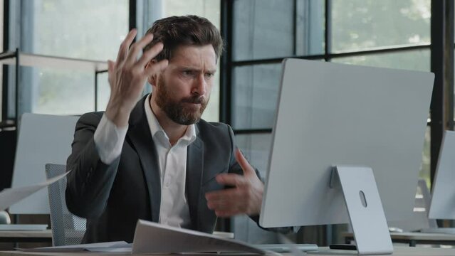Adult bearded Caucasian angry businessman tired unhappy mad man sit at desk feel stress with paperwork deadline upset trouble with work throwing papers hate job nerves difficult startup worry