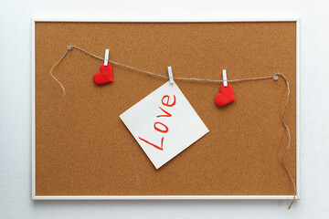 Selective focus on the wall on which red hearts and a leaflet with the inscription love hang on a cork board on a jute rope on white clothespins, mockup.