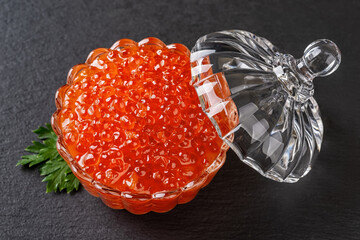 Salmon caviar in a crystal bowl with lid over black background. Glass dish full of chum red caviar close-up. Salted salmon roe for gourmet food concept. Seafood fish delicacy.