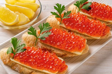 Sandwiches with red caviar on a white plate. Gourmet appetizer of trout caviar on a slice of french...