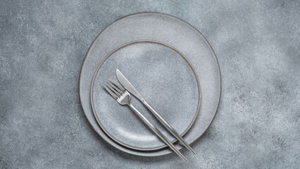 Gray plates with cutlery on a gray concrete background. Minimal table setting. Trendy ceramic dishes. Top view, flat lay, banner.
