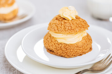 Craquelin Choux biscuits with cream vanilla filling pored with chocolate on light grey background....