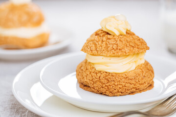 Craquelin Choux biscuits with cream vanilla filling pored with chocolate on light grey background. Traditional french pastry and dessert
