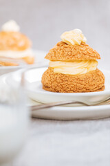 Craquelin Choux biscuits with cream vanilla filling pored with chocolate on light grey background. Traditional french pastry and dessert