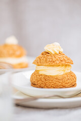 Craquelin Choux biscuits with cream vanilla filling pored with chocolate on light grey background. Traditional french pastry and dessert