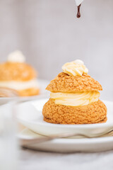 Craquelin Choux biscuits with cream vanilla filling pored with chocolate on light grey background. Traditional french pastry and dessert