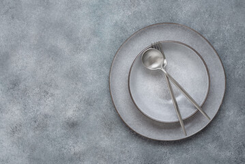 Fototapeta na wymiar Gray plates and silvery cutlery on a gray grunge background. Serving utensils. Top view, copy space. Modern craft ceramic tableware.