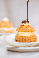 Craquelin Choux biscuits with cream vanilla filling pored with chocolate on light grey background....