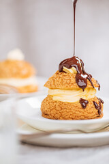 Craquelin Choux biscuits with cream vanilla filling pored with chocolate on light grey background. Traditional french pastry and dessert