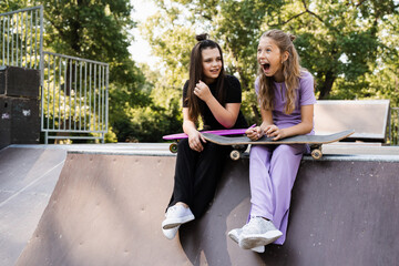Sporty children girls with skateboard and penny boards are sitting and chatting with each other on sports ramp on playground. Friends communication and friendship. Sports extreme lifestyle. © Rabizo Anatolii