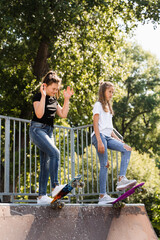 Naklejka na ściany i meble Children friendship. Girls friends ready for ride on penny board on skateboard park playground. Sports equipment for kids. Extreme lifestyle.