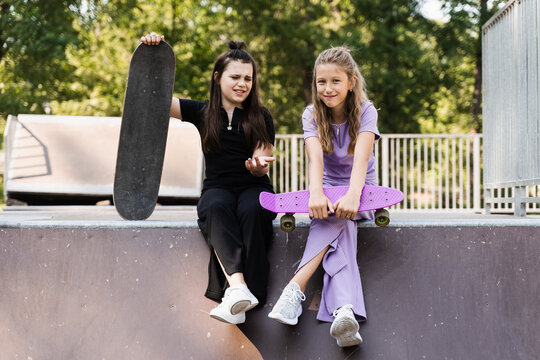 Kids girls smile and laugh and have fun together. Children with skateboard and penny boards communicate and discuss on the sports playground. Girls friendship concept.