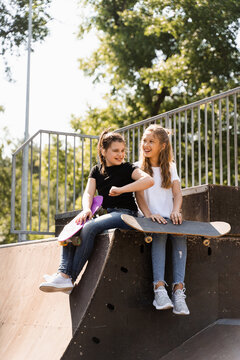 Kids girls smile and laugh and have fun together. Children with skateboard and penny boards communicate and discuss on the sports playground. Girls friendship concept.