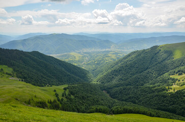Fototapeta na wymiar Summer nature landscape, view from the mountain range to the valley covered with forest and village from the distance. Carpathian Mountains, Ukraine