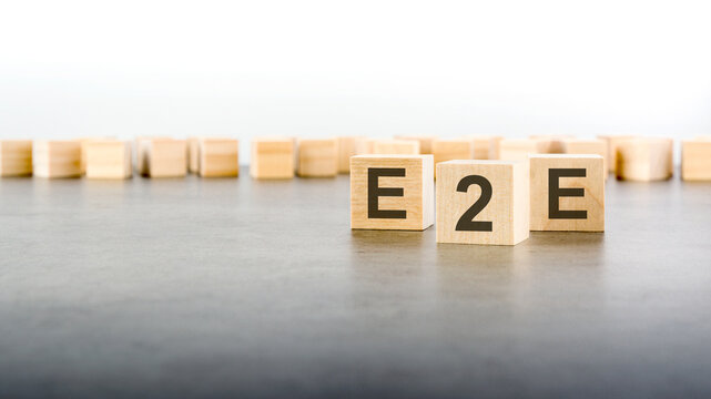 three wooden cubes with the letters E2E on the bright surface of a gray table
