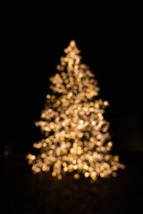 Silhouette of blurry Christmas tree illuminated and decorated with golden fairy lights in dark...
