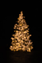 Silhouette of blurry Christmas tree illuminated and decorated with golden fairy lights in dark night creating beautiful bokeh effect with glowing circles or shiny dots, abstract image for holiday card - 523646467