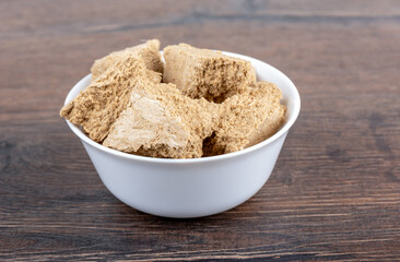 Pieces of halva in a white porcelain bowl over a wooden background.