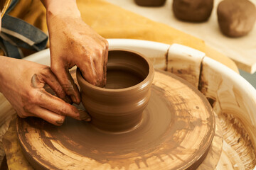 A Potter works with red clay on a Potter's wheel in the workshop..Women's hands create a pot. Girl sculpts in clay pot closeup. Modeling clay close-up. 