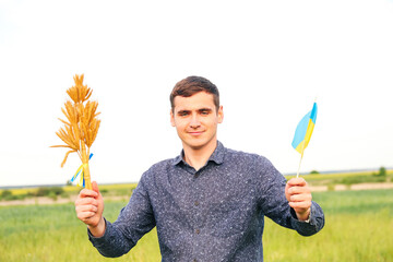 Defocus young man holding ukrainian flag and wheat spikes of wheat tied and flag on the meadow...
