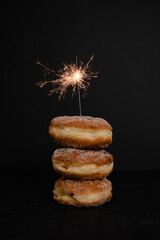 Traditional German or Austrian doughnut typically served for carnival or New Year's Eve filled with rose hip jam and dusted with cinnamon and sugar with sparkler on black background - 523650037
